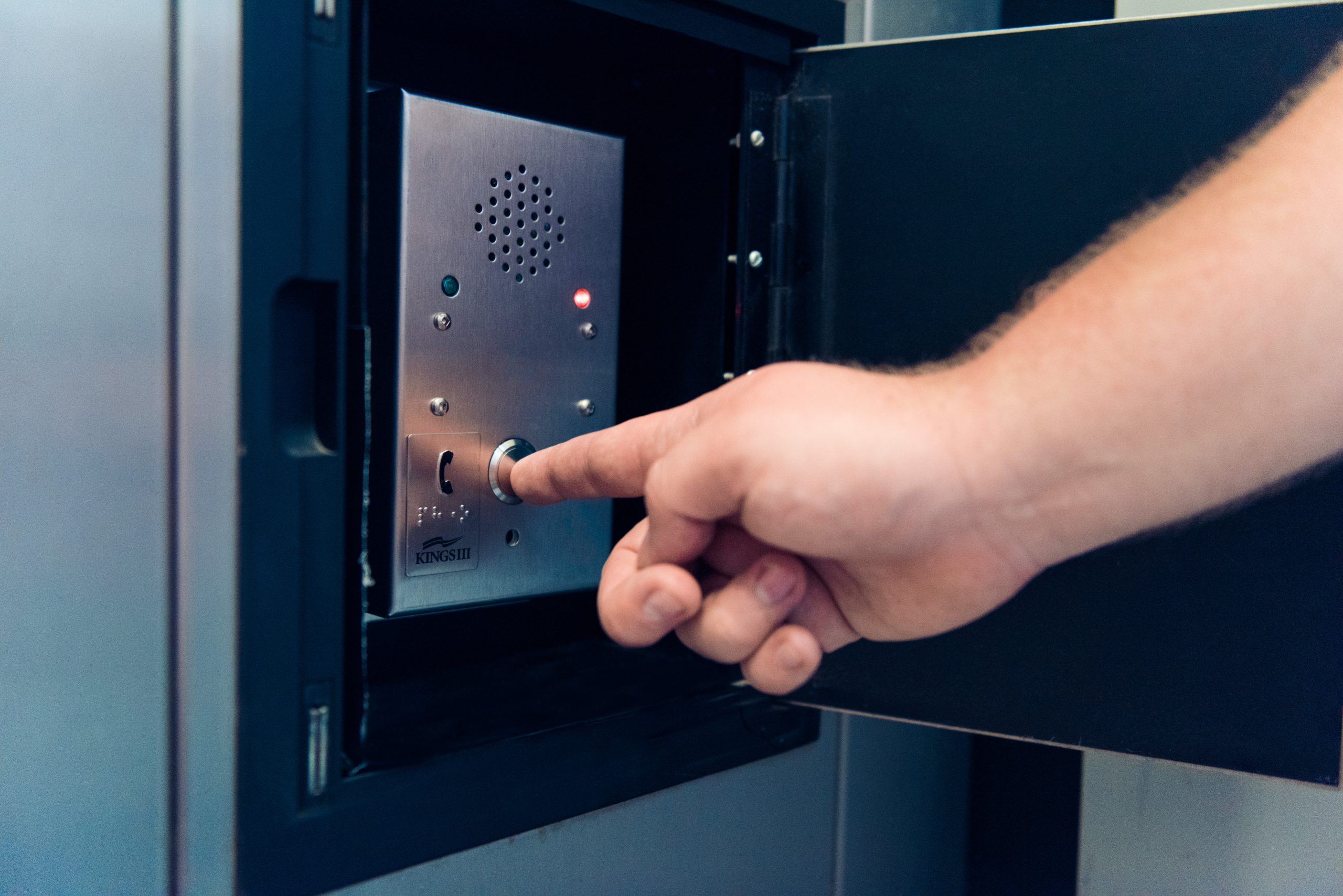 a hand reaches to press a button against the elevator wall to call for an emergency dispatcher