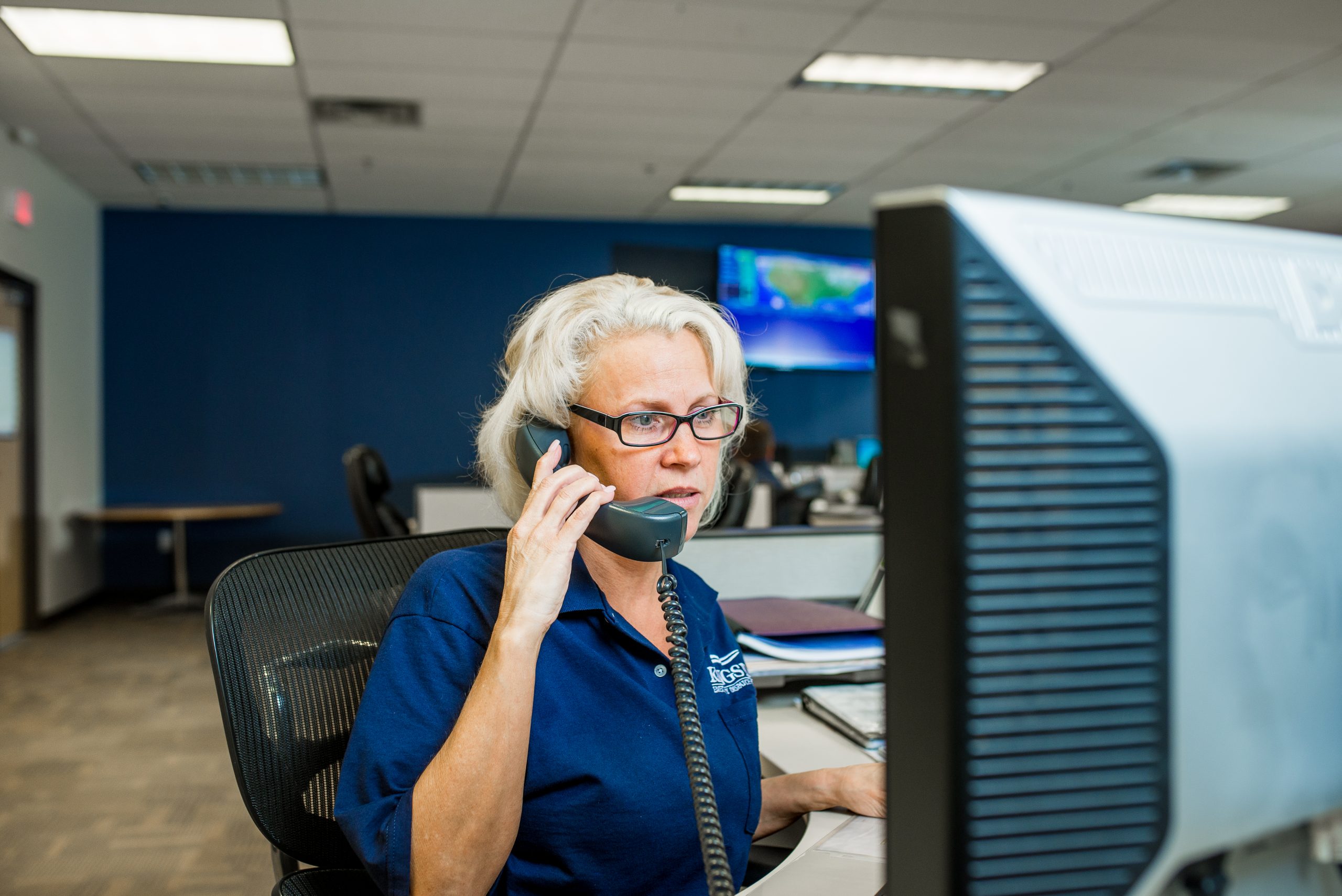 Emergency Dispatcher responding to a call Focused Emergency Dispatcher with glasses, talking on the phone while working at a computer in a modern office.
