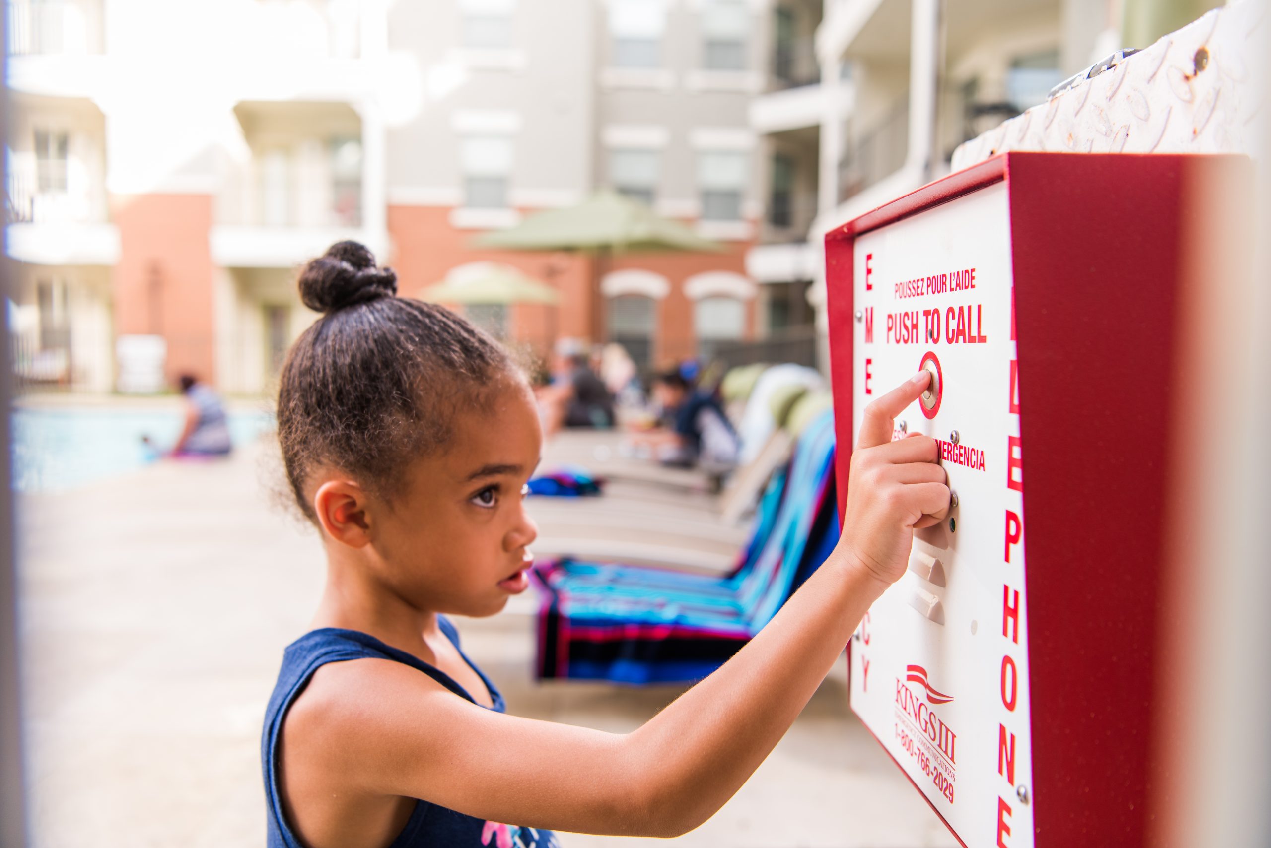 A young girl standing near a emergency pool phone and pushes the button on a sunny day